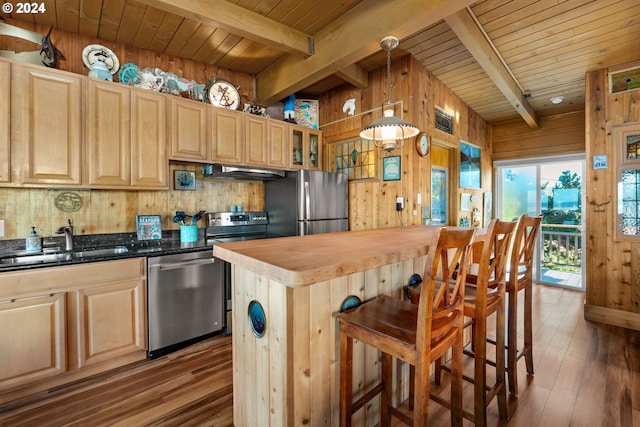 kitchen with wood-type flooring, stainless steel appliances, extractor fan, wooden walls, and hanging light fixtures