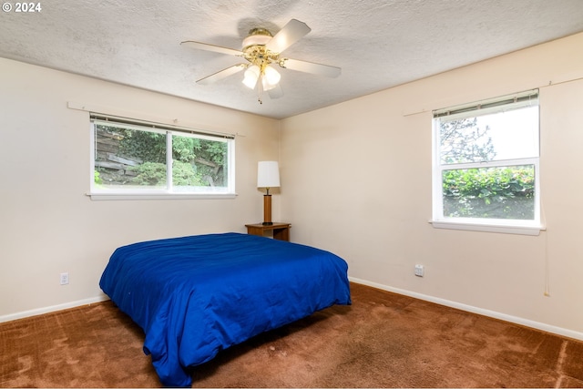 bedroom featuring multiple windows, a textured ceiling, dark carpet, and ceiling fan