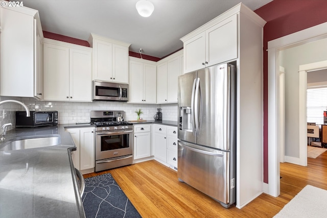 kitchen with light wood-type flooring, appliances with stainless steel finishes, decorative backsplash, and white cabinets