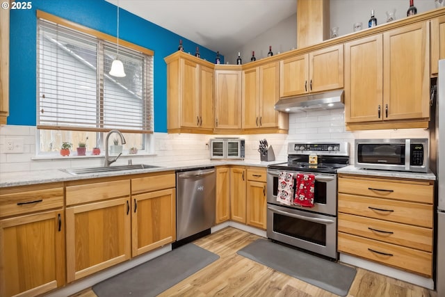 kitchen with hanging light fixtures, sink, light hardwood / wood-style flooring, light stone countertops, and appliances with stainless steel finishes