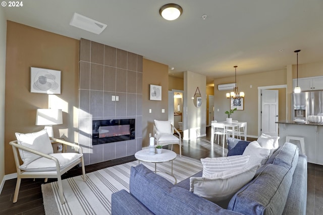 living room featuring an AC wall unit, a tile fireplace, dark hardwood / wood-style floors, and a notable chandelier