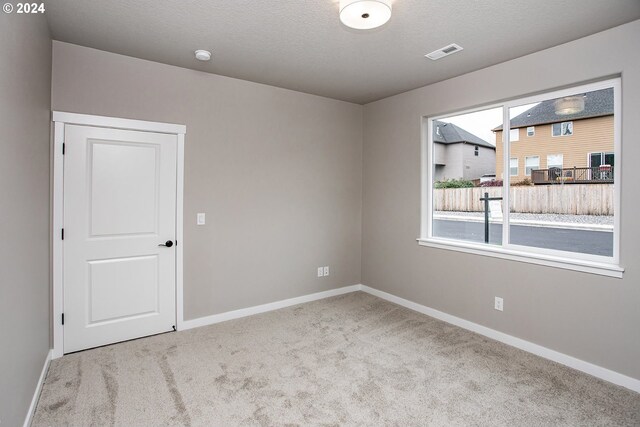 carpeted spare room featuring visible vents, a textured ceiling, and baseboards