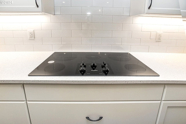 room details featuring light stone counters, tasteful backsplash, black electric cooktop, and white cabinets