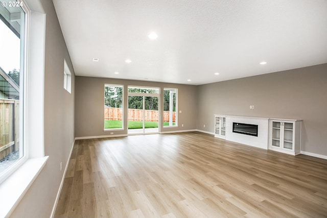 unfurnished living room with recessed lighting, a glass covered fireplace, light wood-style flooring, and baseboards