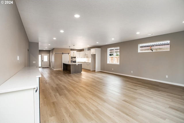 unfurnished living room with baseboards, a barn door, recessed lighting, and light wood-style floors