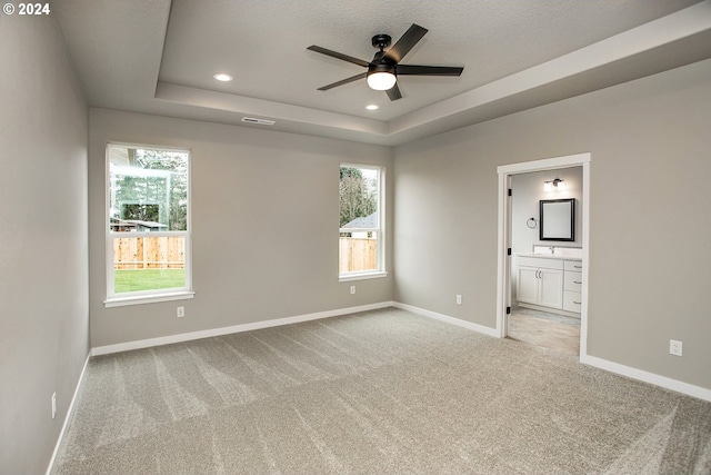 unfurnished bedroom with a tray ceiling, multiple windows, carpet flooring, and baseboards