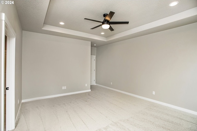 empty room with a tray ceiling, recessed lighting, carpet flooring, a textured ceiling, and baseboards