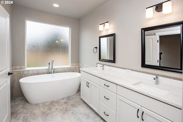 full bath featuring a wainscoted wall, double vanity, a soaking tub, and a sink