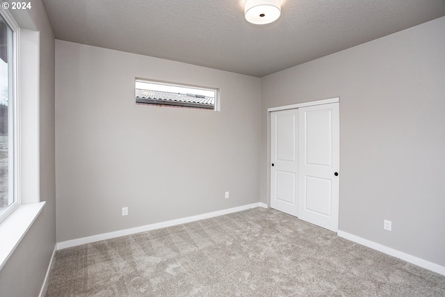 unfurnished bedroom featuring a textured ceiling, a closet, carpet, and baseboards