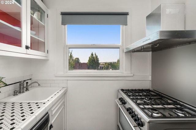 kitchen featuring sink, white cabinetry, stainless steel range with gas cooktop, dishwashing machine, and wall chimney range hood