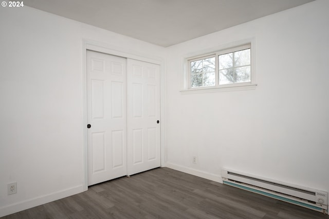 unfurnished bedroom with dark hardwood / wood-style flooring, a baseboard radiator, and a closet