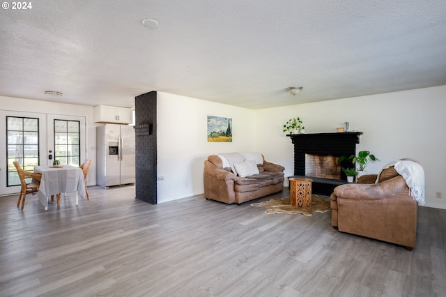 living room with a textured ceiling, light hardwood / wood-style floors, and a brick fireplace