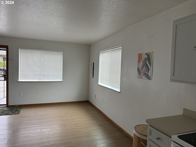 9845 N Lombard St, Portland, OR 97203 - unfurnished dining area with light wood-style floors, a textured ceiling, and baseboards