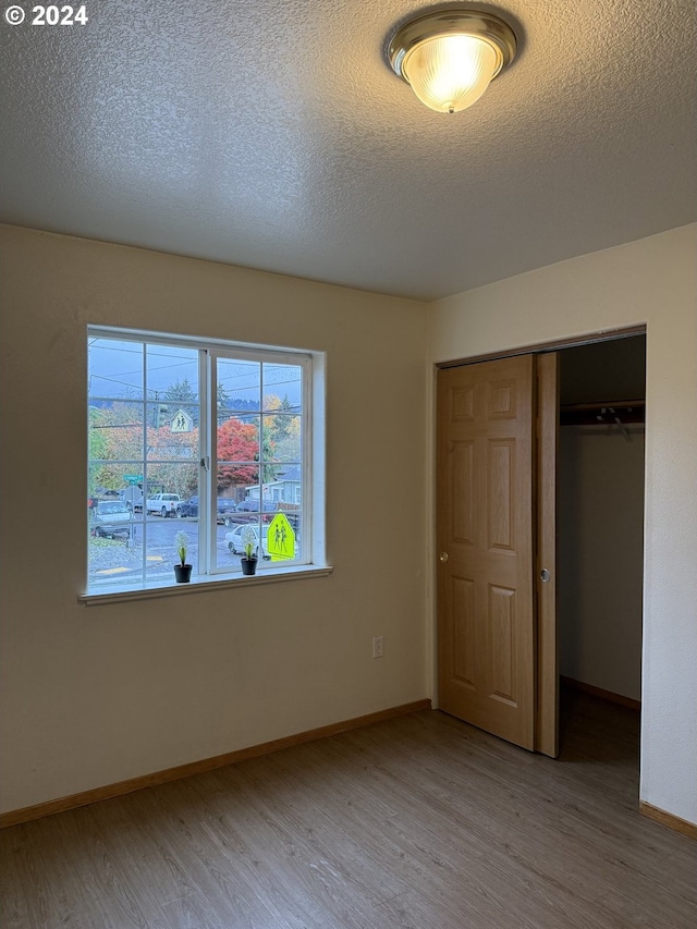9845 N Lombard St, Portland, OR 97203 - unfurnished bedroom with wood finished floors, a closet, a textured ceiling, and baseboards