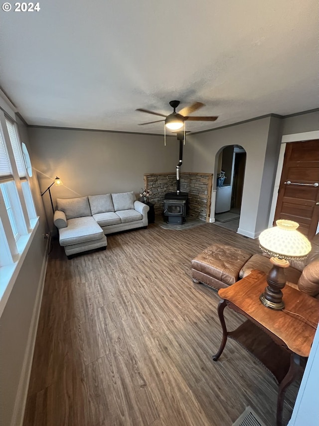 unfurnished living room with baseboards, arched walkways, a ceiling fan, wood finished floors, and a wood stove