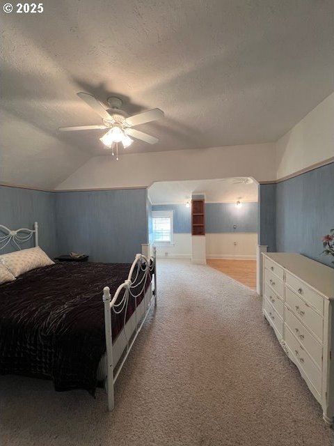 bedroom featuring a ceiling fan, vaulted ceiling, a textured ceiling, and light colored carpet