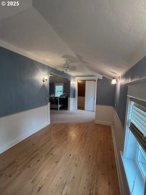 additional living space with a wainscoted wall, ceiling fan, vaulted ceiling, a textured ceiling, and wood finished floors