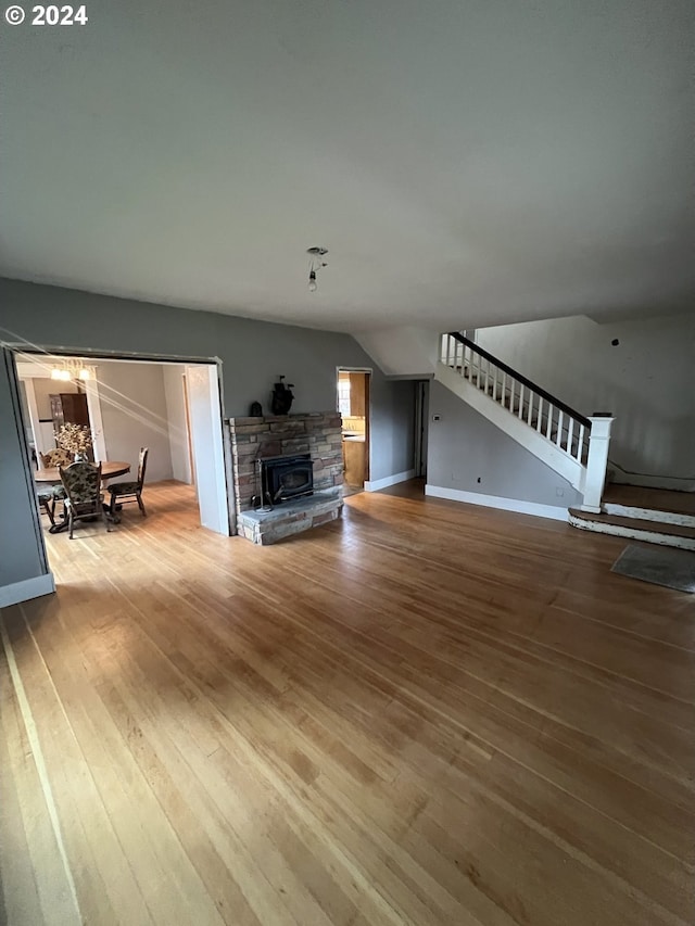 unfurnished living room with baseboards, stairway, wood finished floors, vaulted ceiling, and a stone fireplace