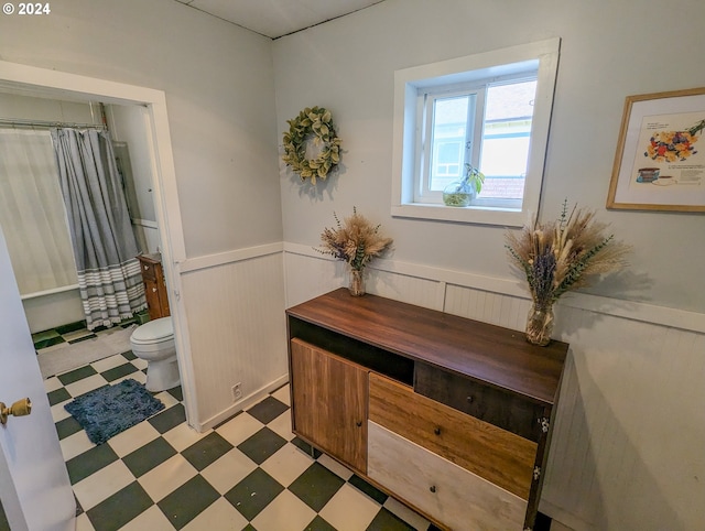 interior space featuring tile patterned floors, a wainscoted wall, curtained shower, and toilet