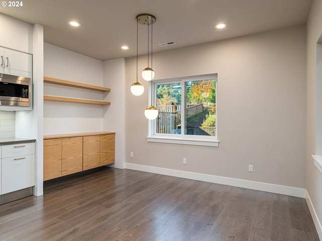 kitchen with dark hardwood / wood-style floors, stainless steel microwave, white cabinets, and decorative light fixtures