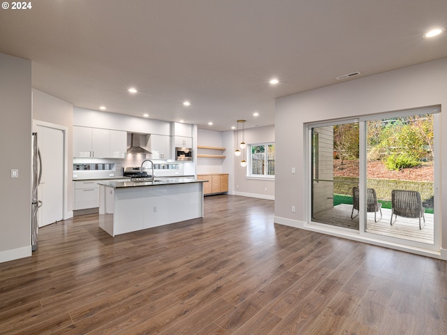 kitchen with sink, hanging light fixtures, an island with sink, white cabinets, and wall chimney range hood