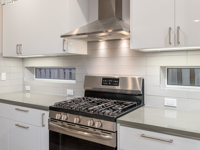 kitchen with ventilation hood, white cabinetry, dark stone countertops, decorative backsplash, and gas range