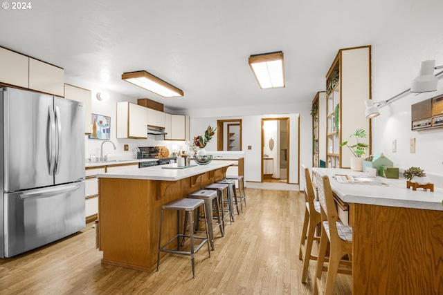 kitchen with a breakfast bar area, light countertops, light wood-style floors, stainless steel appliances, and a sink