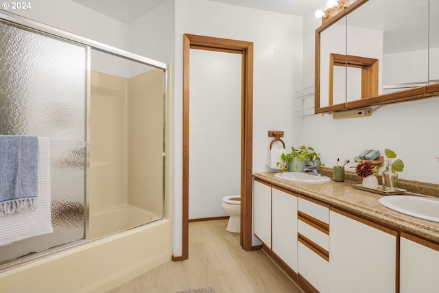 full bath featuring toilet, a sink, wood finished floors, double vanity, and enclosed tub / shower combo