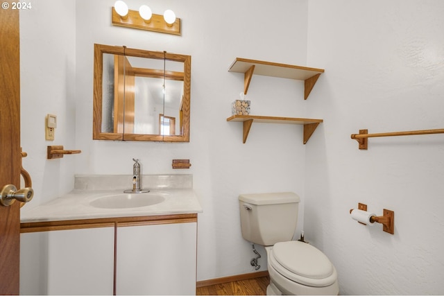 half bathroom with toilet, vanity, baseboards, and wood finished floors