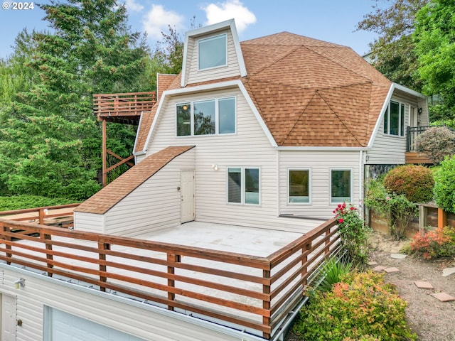 rear view of property with a wooden deck, a balcony, and a shingled roof