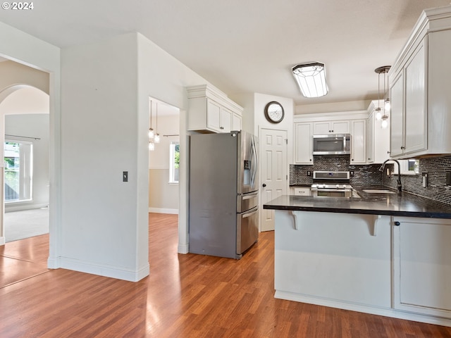 kitchen with white cabinets, sink, appliances with stainless steel finishes, decorative light fixtures, and kitchen peninsula