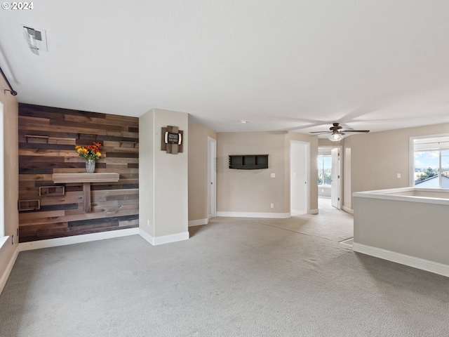 unfurnished living room featuring wood walls, ceiling fan, and light carpet