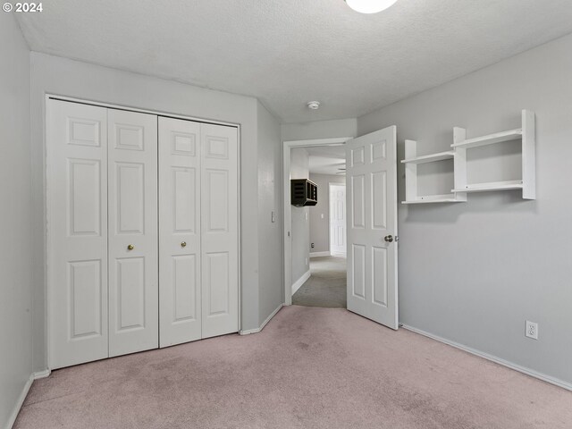 unfurnished bedroom featuring light carpet, a textured ceiling, an AC wall unit, and a closet