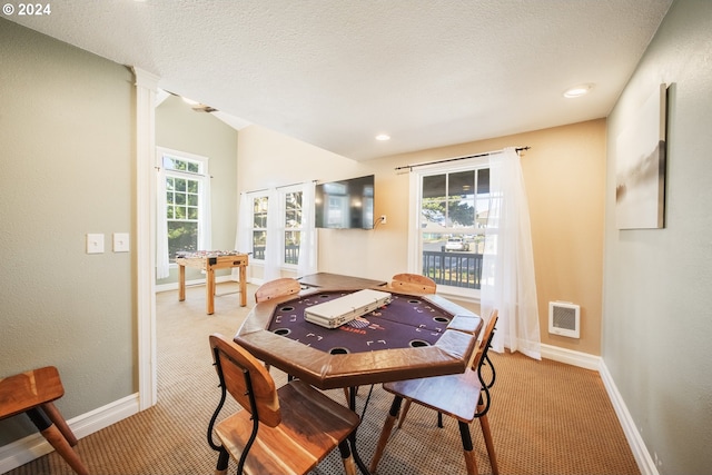 dining area featuring a textured ceiling, light colored carpet, decorative columns, and lofted ceiling