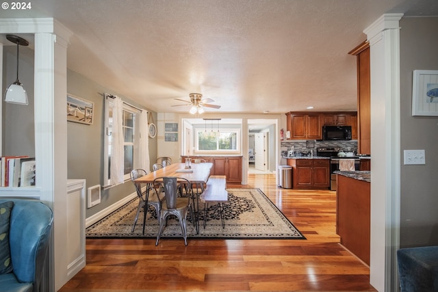 dining space featuring a textured ceiling, light hardwood / wood-style floors, ornate columns, and ceiling fan