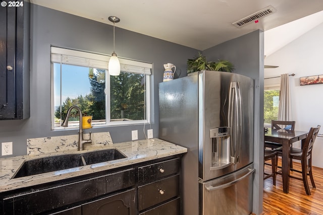 kitchen with light hardwood / wood-style floors, vaulted ceiling, light stone counters, sink, and stainless steel fridge with ice dispenser