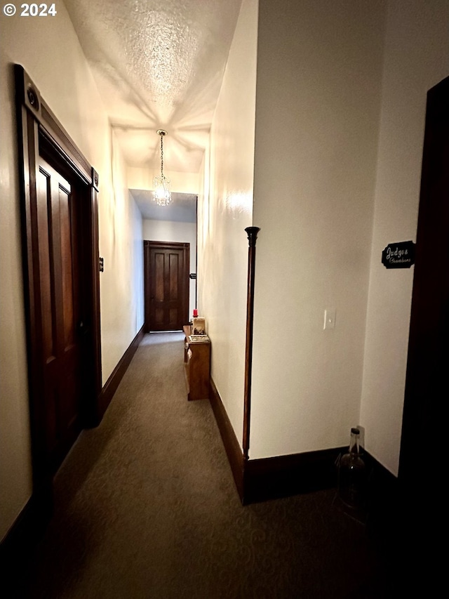 hall with carpet flooring, a textured ceiling, and a chandelier