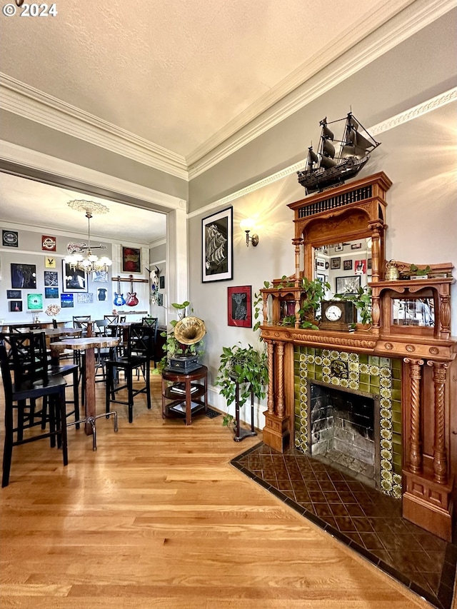 dining room with hardwood / wood-style floors, an inviting chandelier, ornamental molding, a textured ceiling, and a tiled fireplace