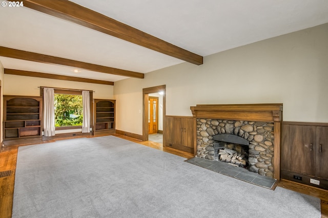 unfurnished living room with beam ceiling, light colored carpet, a fireplace, and wooden walls