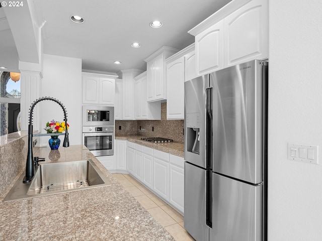 kitchen featuring decorative backsplash, stainless steel appliances, sink, light tile patterned floors, and white cabinets