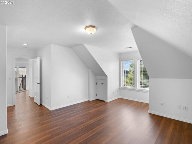 additional living space with a textured ceiling, dark wood-type flooring, and vaulted ceiling