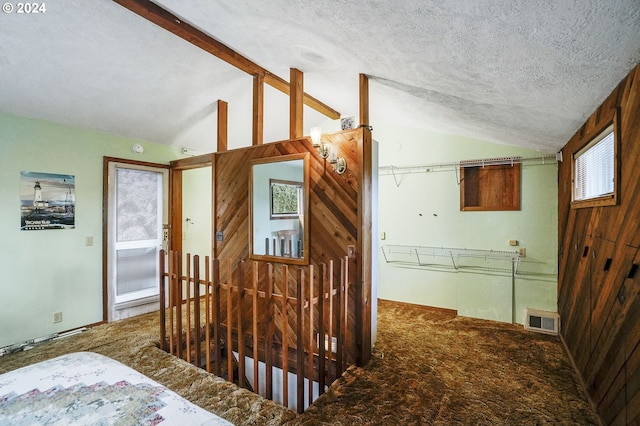 hall with a textured ceiling, dark carpet, and vaulted ceiling with beams