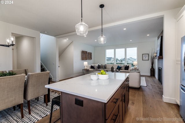 kitchen with a breakfast bar, light stone counters, dark brown cabinetry, light hardwood / wood-style flooring, and hanging light fixtures