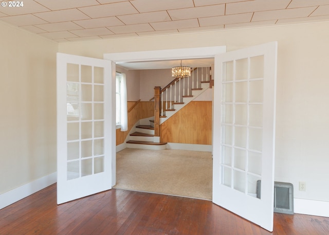 spare room featuring french doors, a notable chandelier, wood-type flooring, and wooden walls