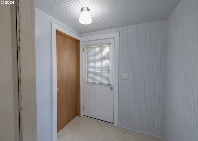 doorway to outside with wooden walls and carpet flooring