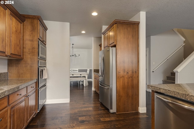 kitchen featuring appliances with stainless steel finishes, dark wood-type flooring, pendant lighting, and a textured ceiling