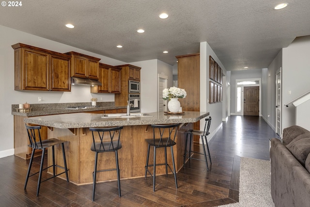 kitchen with a textured ceiling, stainless steel appliances, dark hardwood / wood-style flooring, and a kitchen bar