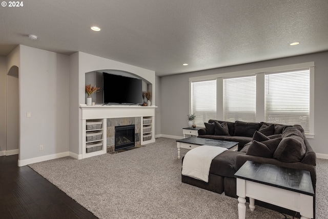 living room with a textured ceiling, dark wood-type flooring, and a tiled fireplace