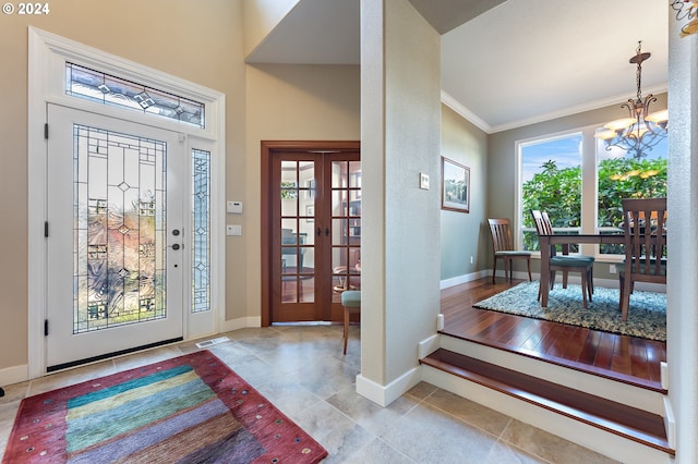 foyer featuring french doors, light hardwood / wood-style floors, crown molding, and an inviting chandelier