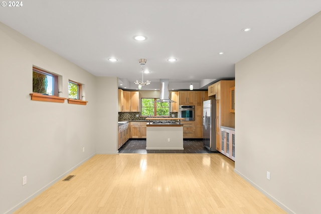 kitchen with appliances with stainless steel finishes, island exhaust hood, hanging light fixtures, light hardwood / wood-style floors, and decorative backsplash